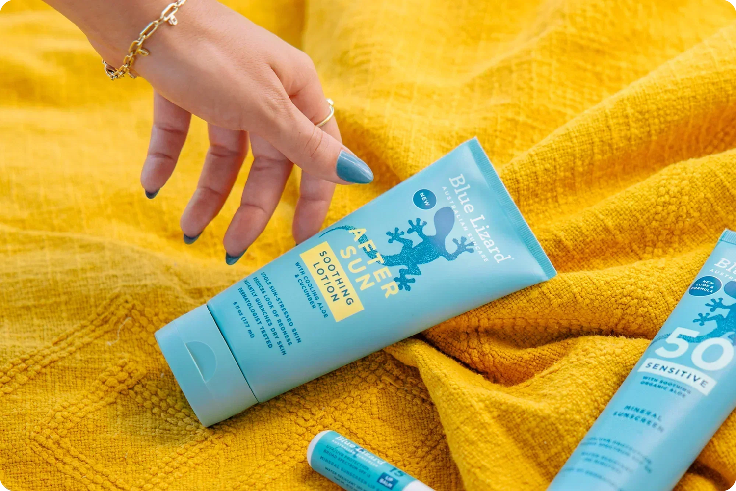 Hand reaching for Blue Lizard After Sun lotion on a yellow blanket background