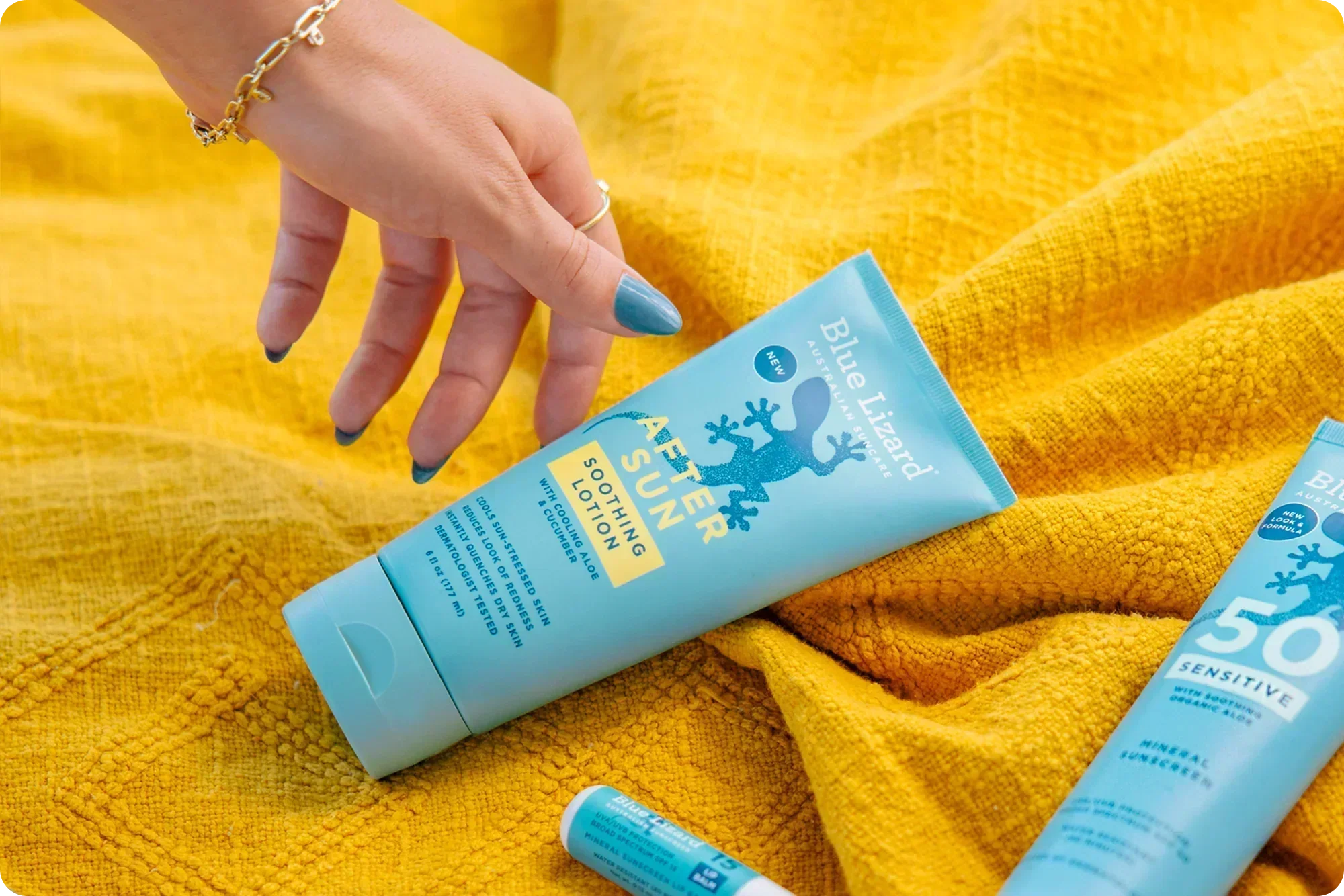 Hand reaching for Blue Lizard After Sun lotion on a yellow blanket background