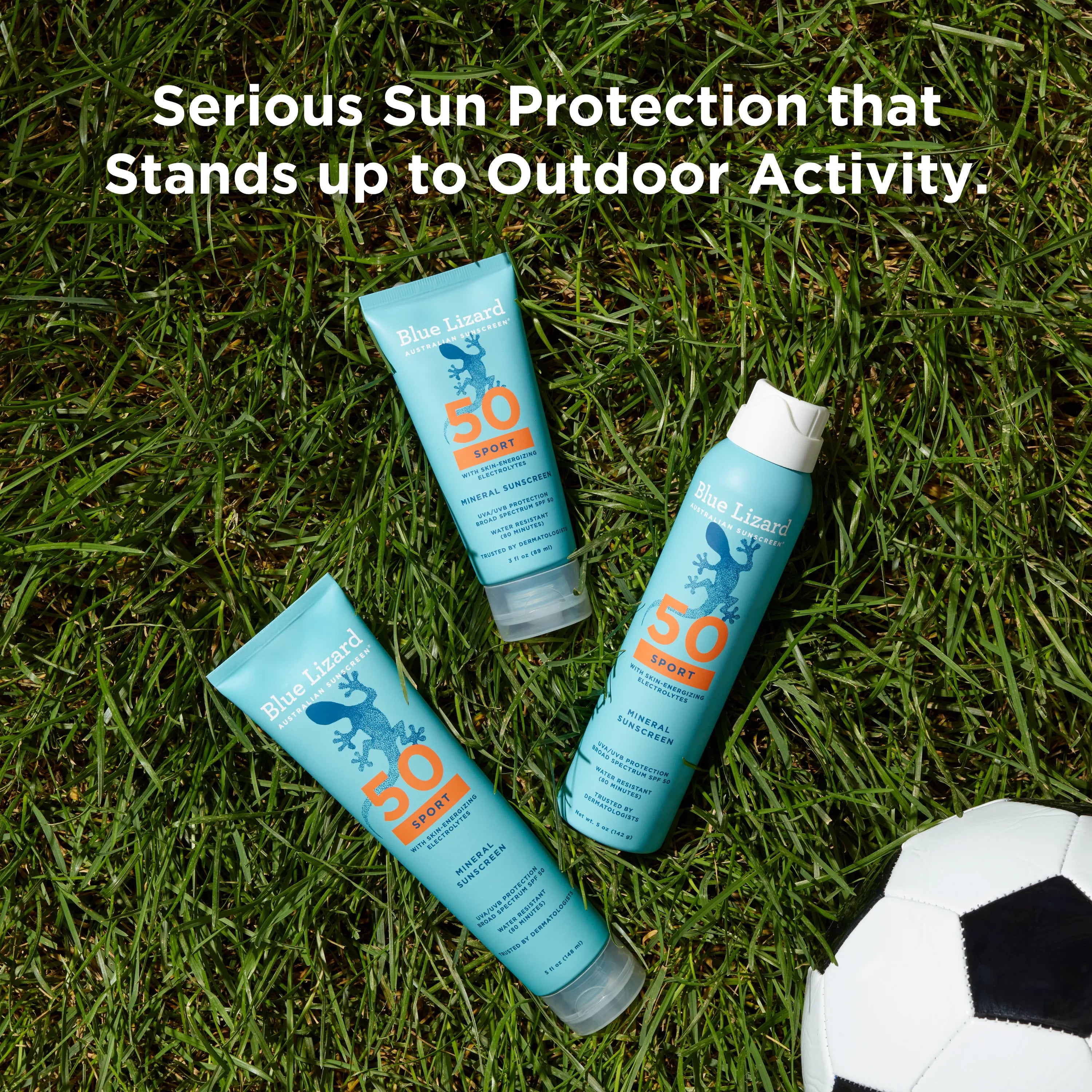 Two tubes and one spray bottle of Blue Lizard Sport SPF 50 mineral sunscreen on grass with a soccer ball