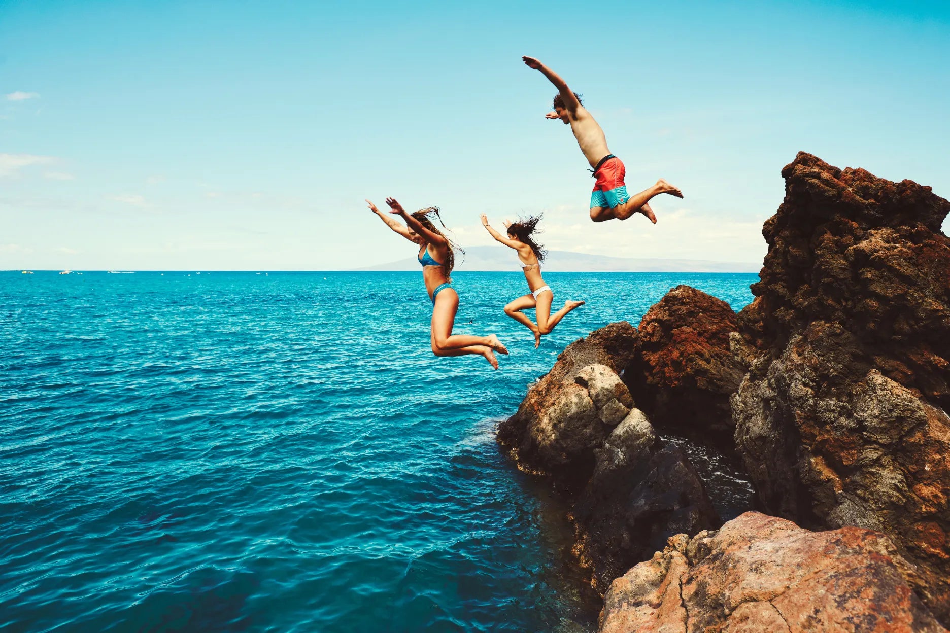 Three people jumping in the water from a rock