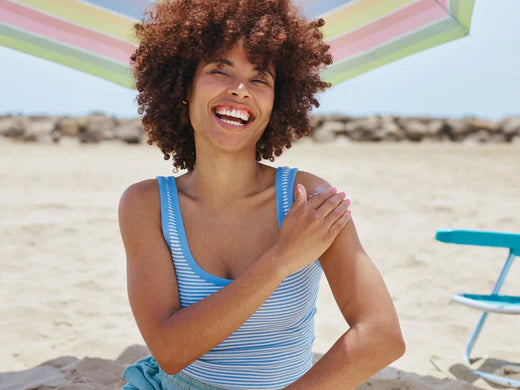 A smiling woman applying on sunscreen on her shoulder