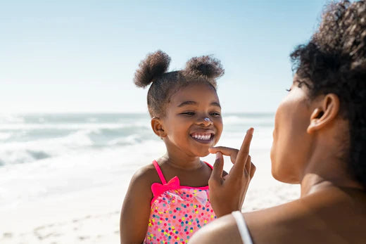 A woman putting on sunscreen on a child's face on the beach