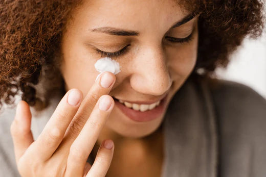 Woman smiling while applying skincare cream under her eyes.