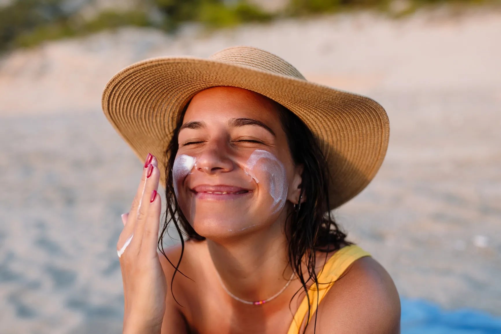 A woman smiling and applying sunscreen on her face