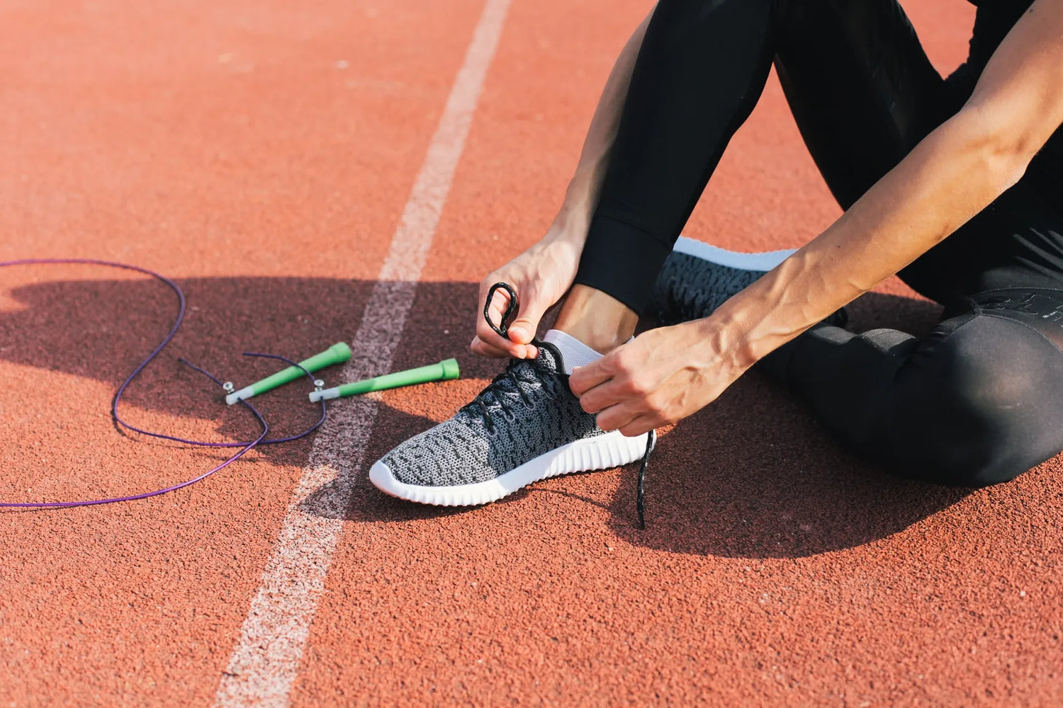 Person tying shoelaces on a track with a jump rope nearby