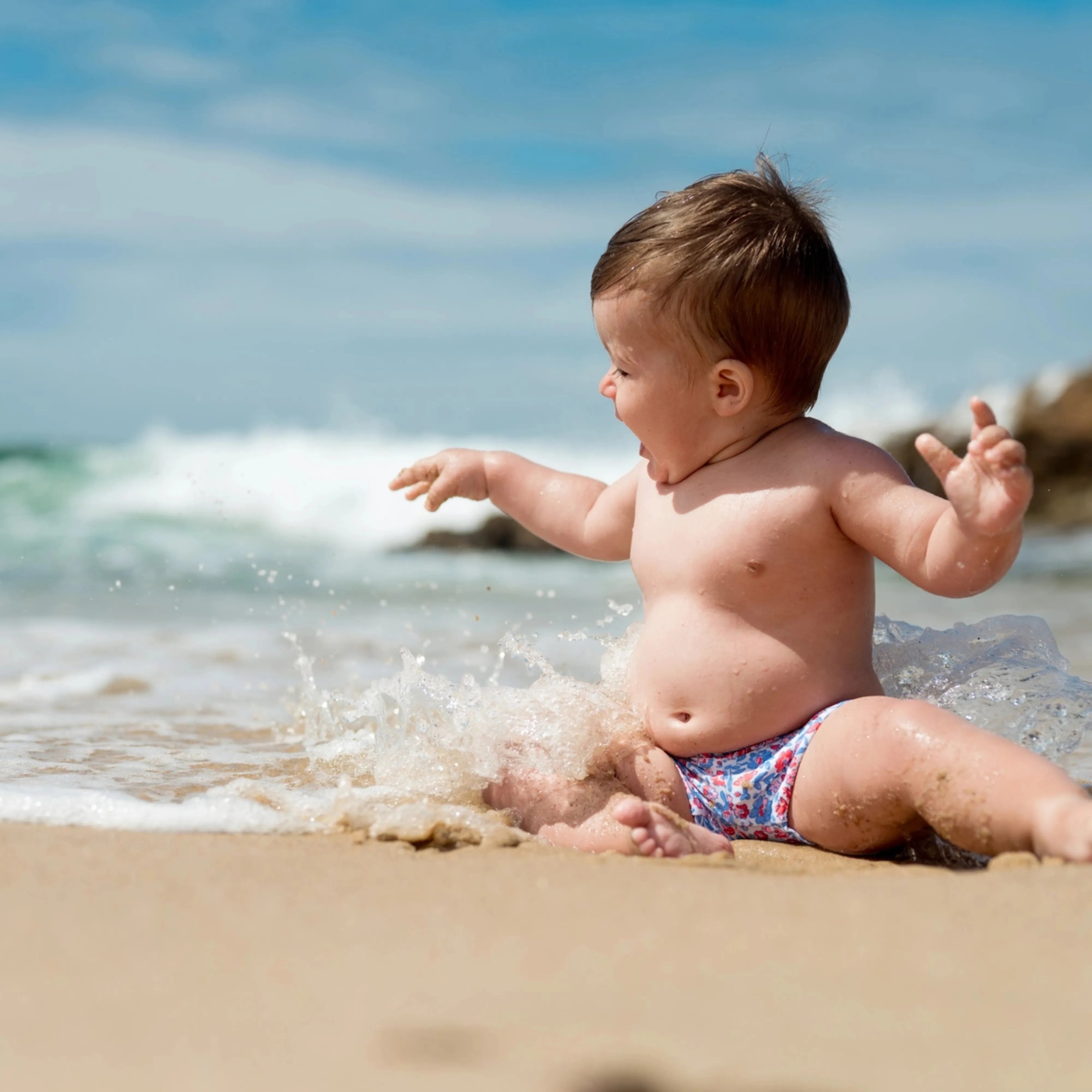 Baby playing at the beach with waves splashing.