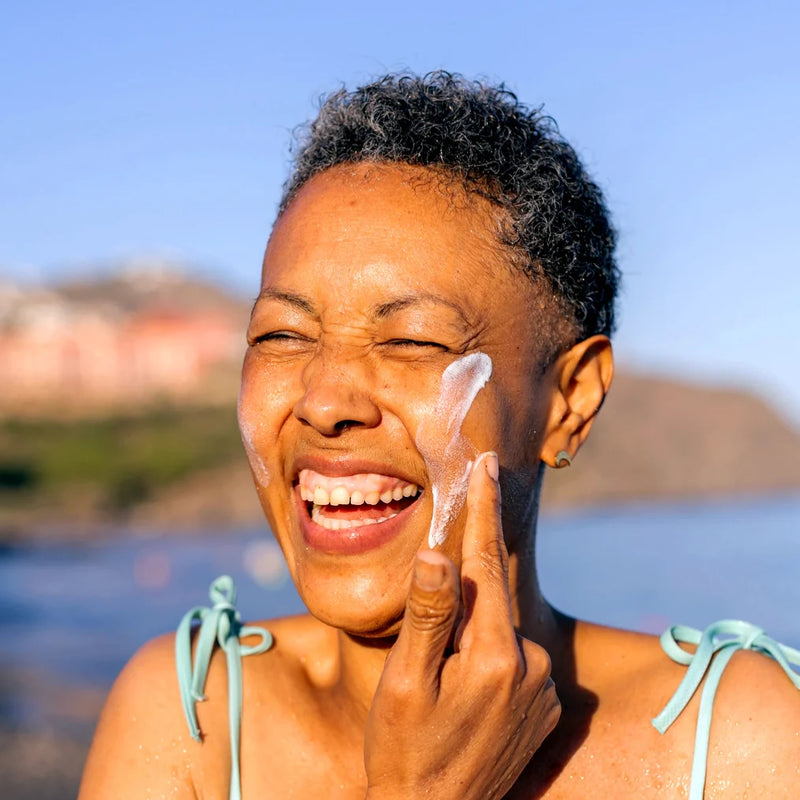 Smiling woman applying Blue Lizard sunscreen on her face