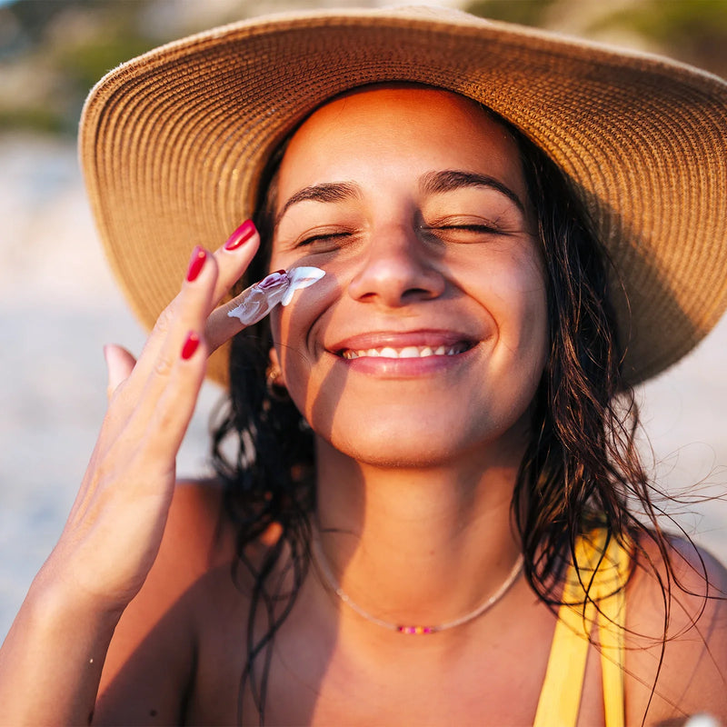 A woman in a sun hat applying Blue Lizard sunscreen on her face