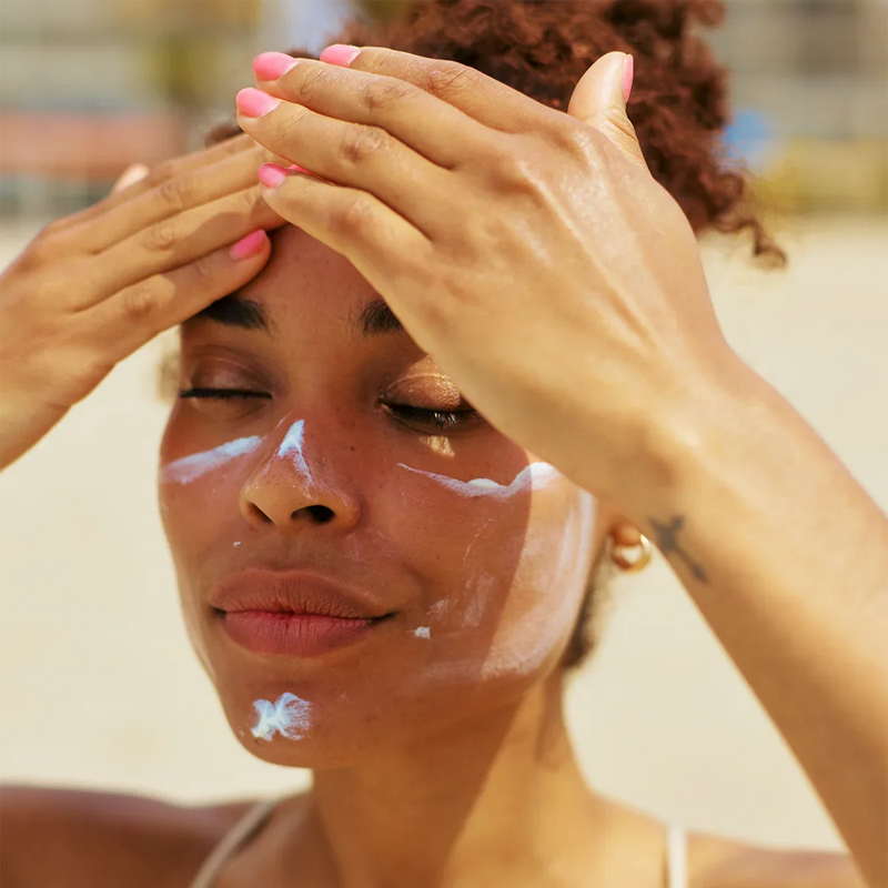 A woman applying Blue Lizard sunscreen on her face on the beach